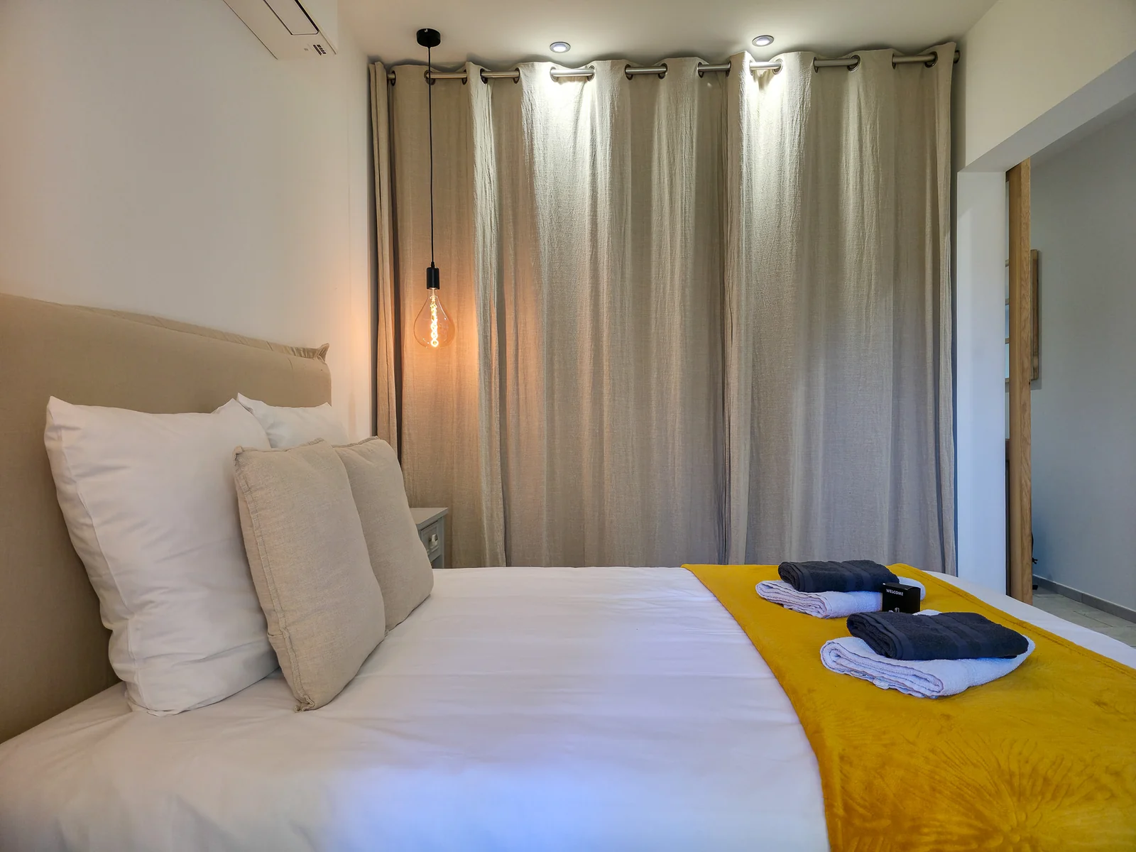 Chambre avec lit préparé, couvre-lit jaune et rideaux clairs