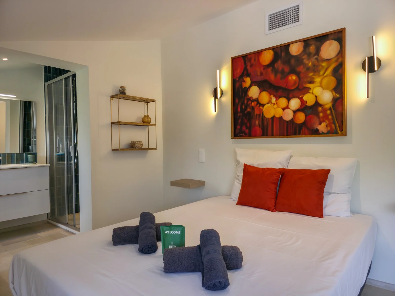 Chambre avec linge blanc, coussins terracotta et tableau coloré