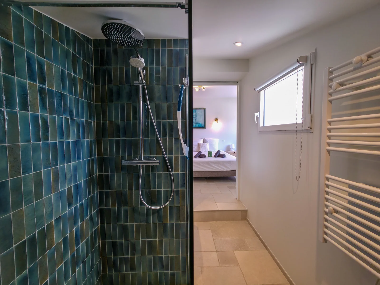 Salle d’eau avec douche carrelée de bleu et sèche-serviettes blanc